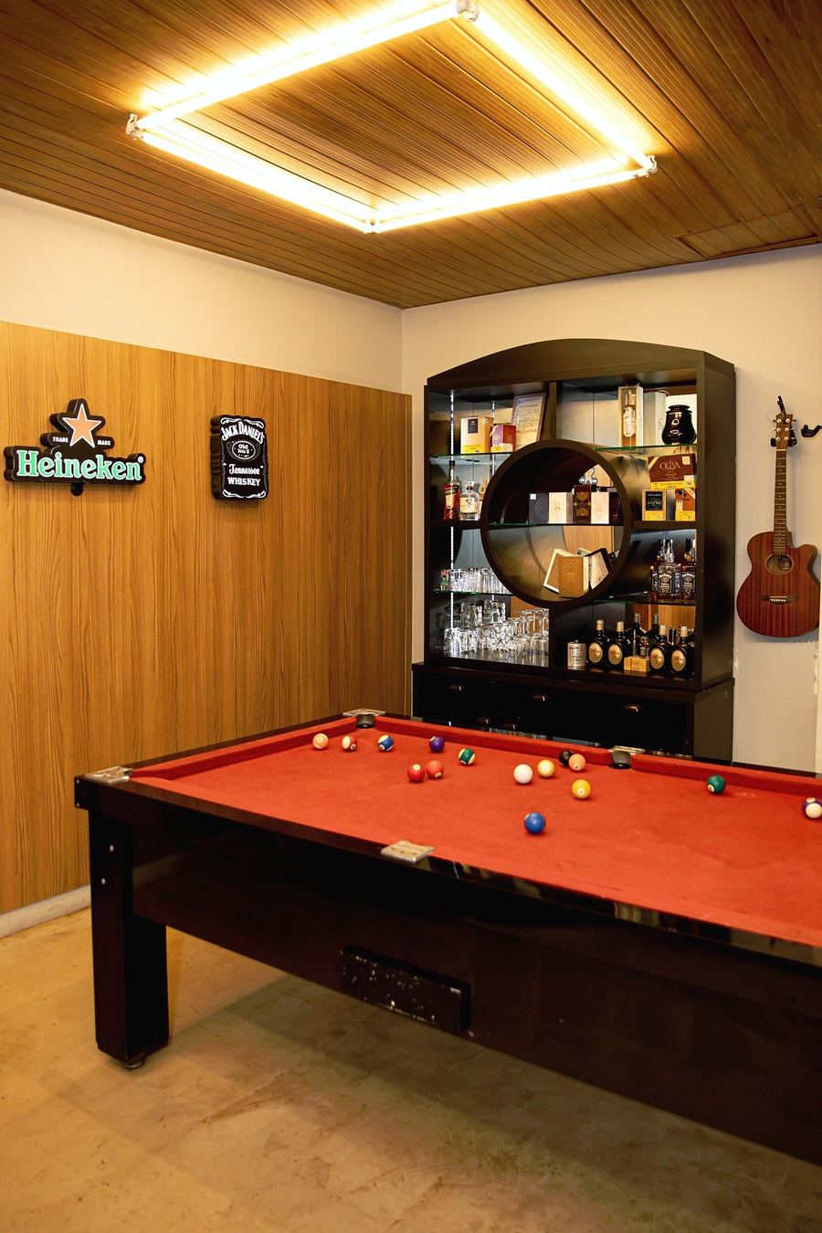 Sala com mesa de sinuca, estante de bebidas e violão